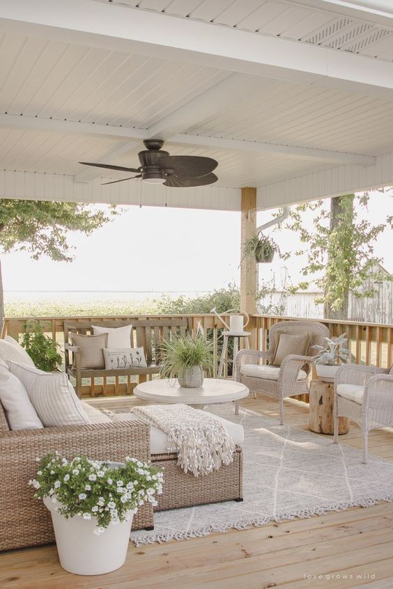 a beautiful neutral modern farmhouse terrace with neutral wicker furniture, a round coffee table, potted plants and blooms
