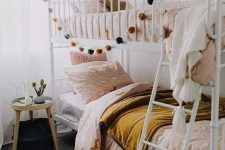 a boho shared girls’ bedroom with a metal bunk bed, pink and mustard bedding, a round side table and pendant lamps