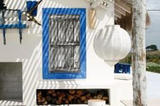 a bold white and blue beach patio with framed shutters, white furniture, striped textiles, a paper lamp and blue accessories