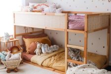 a bright and cool shared girls’ bedroom with a bunk bed with warm-colored bedding, a pouf with pompoms, shelves fro storage and calligraphy