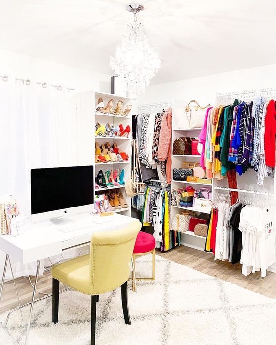 a bright cloffice with a white desk, a yellow chair, a hot pink stool, a makeshift closet, storage shelves with bright clothing and shoes