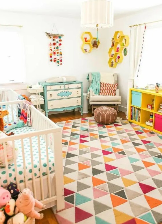 a bright mid century modern nursery with a white crib, a colorful geometric rug, a turquoise dresser, a yellow shelving unit and yellow hexagon shelves