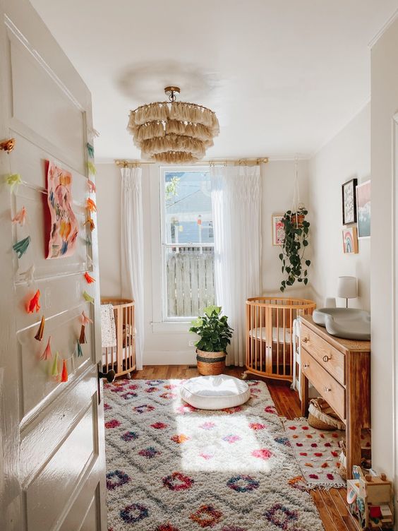 a bright mid-century modern nursery with bold printed rugs, light-stained furniture, a tassel chandelier and potted plants