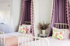 a chic and stylish shared girls’ bedroom with white vintage beds, lilac and peachy bedding, purple canopies, a built-in wardrobe and a woven basket for storage