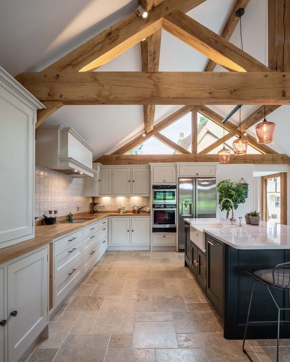 a chic barn kitchen with white shaker style cabinets, a black kitchen island, wooden beams, pendant lamps
