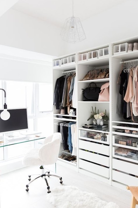a chic contemporary cloffice with a white amekshift closet, drawers, some open shelves, a sheer glass desk, a white chair and an ethereal lamp