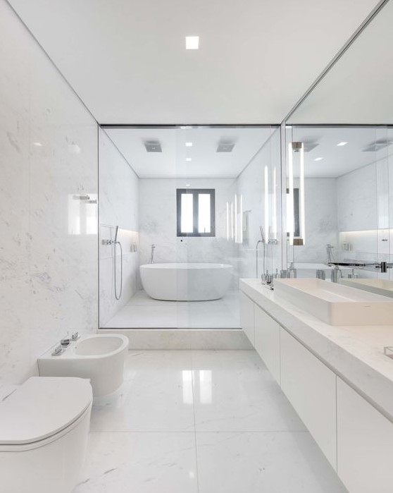 a chic minimalist bathroom clad with large scale white marble tiles, a floating marble vanity and white appliances