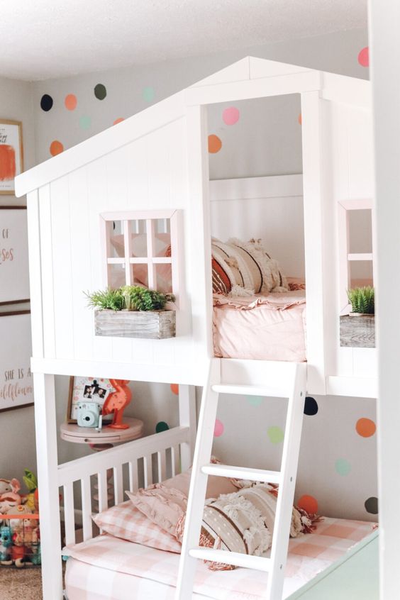 a chic shared bedroom with a house-shaped bunkbed with pink and green bedding, some orange and green touches in decor
