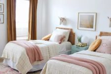 a chic shared girls’ bedroom with a bright printed rug, cane headboard beds with pastel and mustard bedding, mustard curtains and a mint blue nightstand