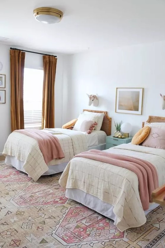 a chic shared girls' bedroom with a bright printed rug, cane headboard beds with pastel and mustard bedding, mustard curtains and a mint blue nightstand