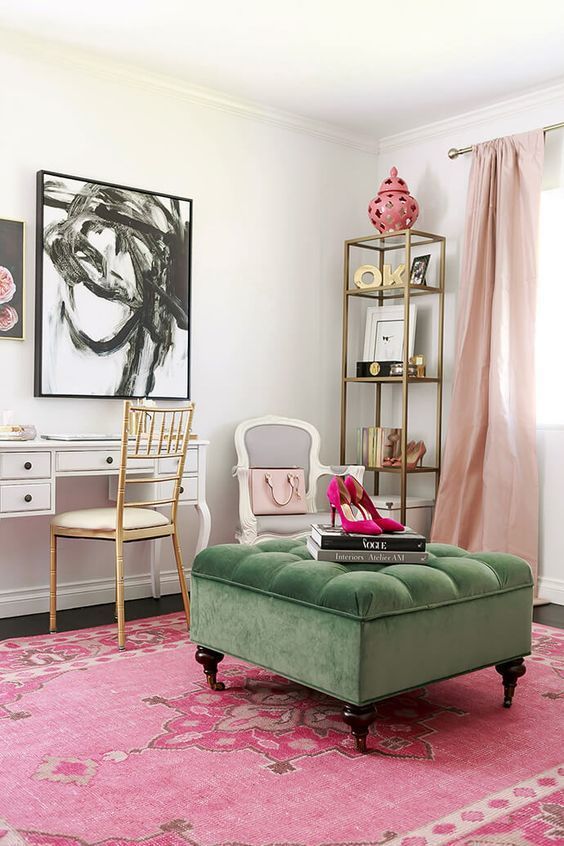 a colorful cloffice with a vintage white desk, a gold chair, a gold shelving unit, a hot pink rug, a green ottoman and blush curtains