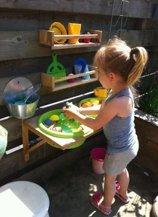 a colorful outdoor kitchen with wooden shelves, colorful plastic tableware and toys for having fun