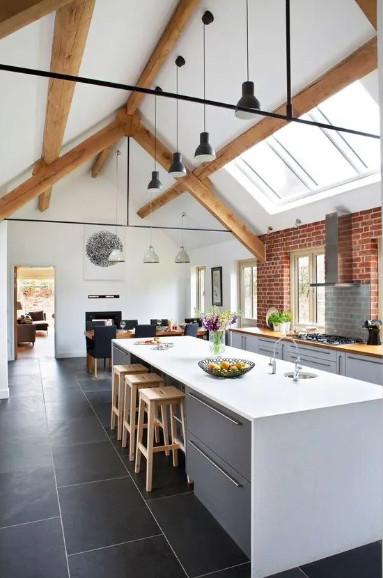 a contemporary barn kitchen with skylights, dove grey plain cabinets, butcherblock countertops, wooden beams, black pendant lamps
