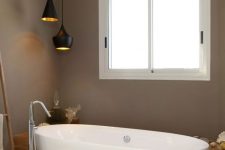a contemporary brown bathroom with a neutral stone tile floor, an oval tub, black pendant lamps