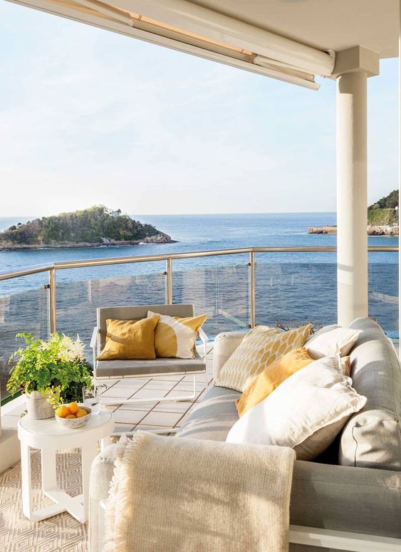 a contemporary seaside terrace with neutral furniture, pillows, a small coffee table and a neutral rug and a lovely sea view