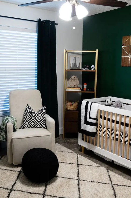 a contrasting mid century modern nursery with a dark green accent wall, a gold shelving unit, a neutral crib, a grey chair, a black pouf and black and white textiles