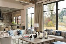 a cool barn living room with a reclaimed wooden ceiling with beams, creamy seating furniture, an antler chandelier, a coffee table and blue stools