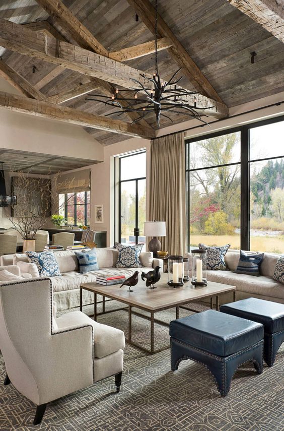 a cool barn living room with a reclaimed wooden ceiling with beams, creamy seating furniture, an antler chandelier, a coffee table and blue stools