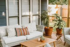 a cool modern country outdoor living room with neutral woven furniture, printed pillows, a wooden table and potted plants welcomes