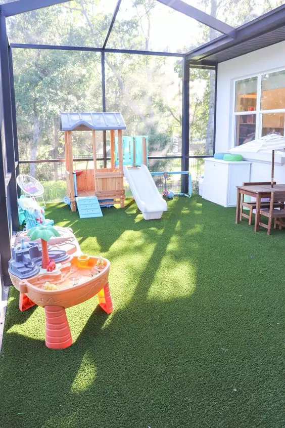 a covered outdoor play area for kids, with a faux lawn, slides, play baths and a beach and some kid furniture is awesome to play in