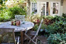 a cozy rustic dining space in the garden under the trees and with greenery around, with a reclaimed wood dining set is a lovely area