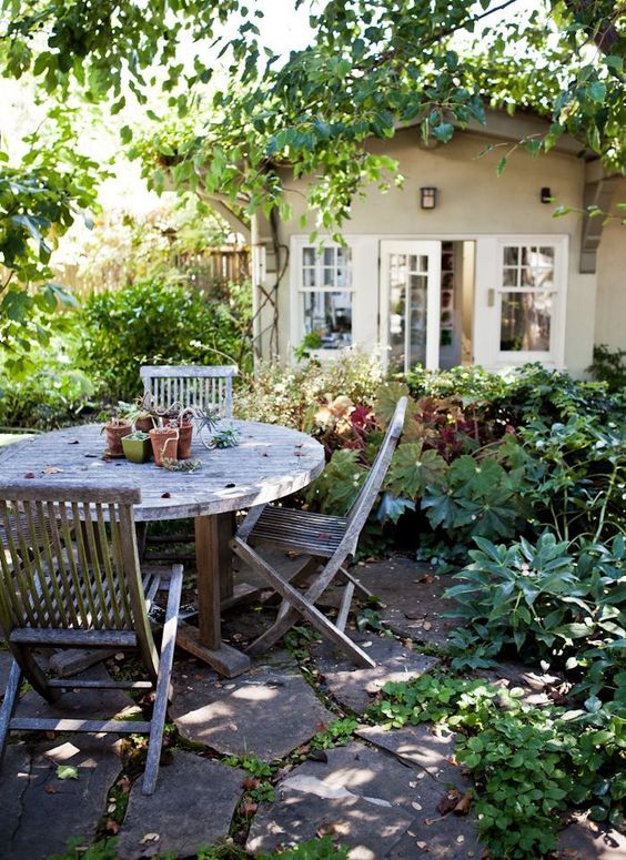 a cozy rustic dining space in the garden under the trees and with greenery around, with a reclaimed wood dining set is a lovely area
