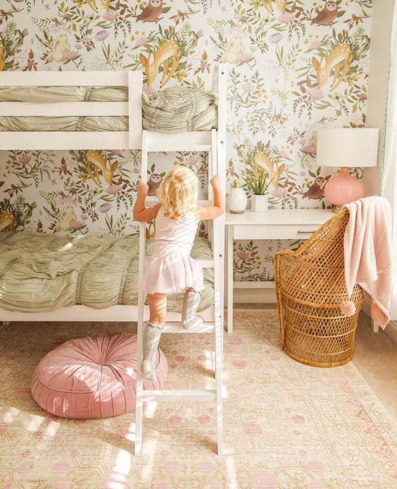 a cozy shared girls' room with a flora and fauna wallpaper wall, a white bunk bed with pastel bedding, a white desk with a rattan chair