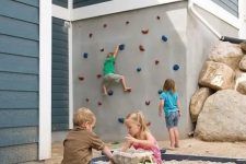 a creative outdoor play space wiht a climbing wall and a sand box with colorful toys