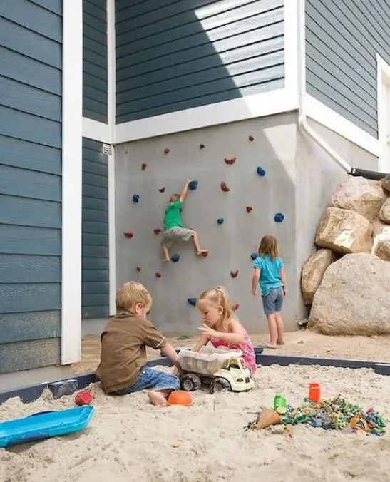 a creative outdoor play space wiht a climbing wall and a sand box with colorful toys