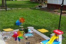 a cute and colorful kids’ play space with pebbles, a mini pond, a slide for dolls and some potted plants and blooms