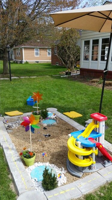 a cute and colorful kids' play space with pebbles, a mini pond, a slide for dolls and some potted plants and blooms