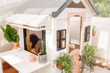 a cute kids’ playhouse in white and pink, with potted greenery, a table is a great idea for a backyard