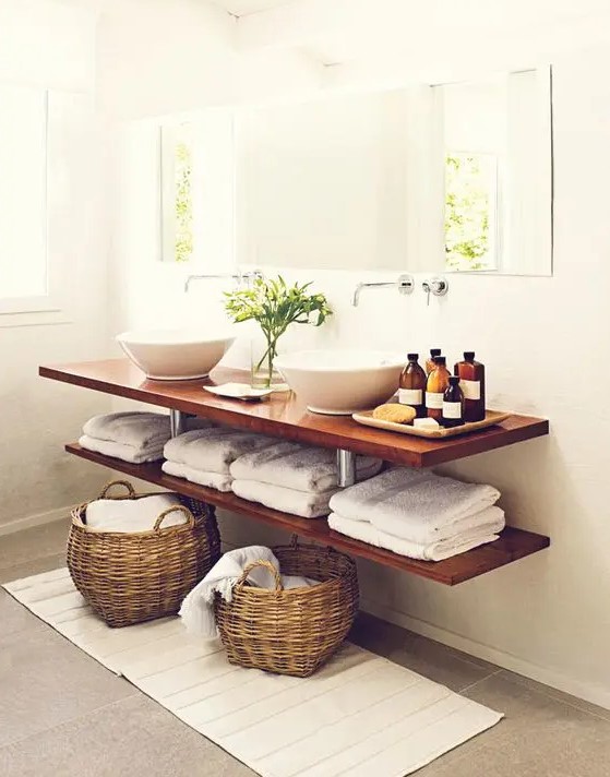 a double floating vanity composed of two stained shelves, with bowl sinks, bottles, towels and baskets for storage