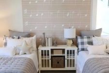 a dreamy neutral shared girls’ bedroom with white beds and a storage unit, grey and white bedding, a music accent wall, a crystal pendant lamp
