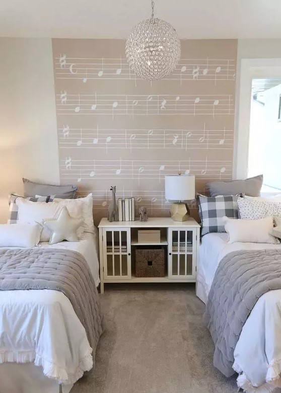 a dreamy neutral shared girls' bedroom with white beds and a storage unit, grey and white bedding, a music accent wall, a crystal pendant lamp