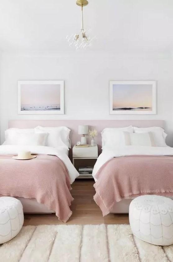 a dreamy shared girls' bedroom with a pink headboard and beds with white and pink bedding, white leather poufs and a nightstand, ocean prints