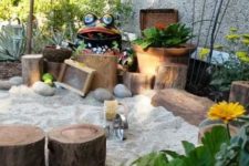 a fun and cute outdoor playground with plants, stumps, sand, pebbles, blooms and some garden figurines