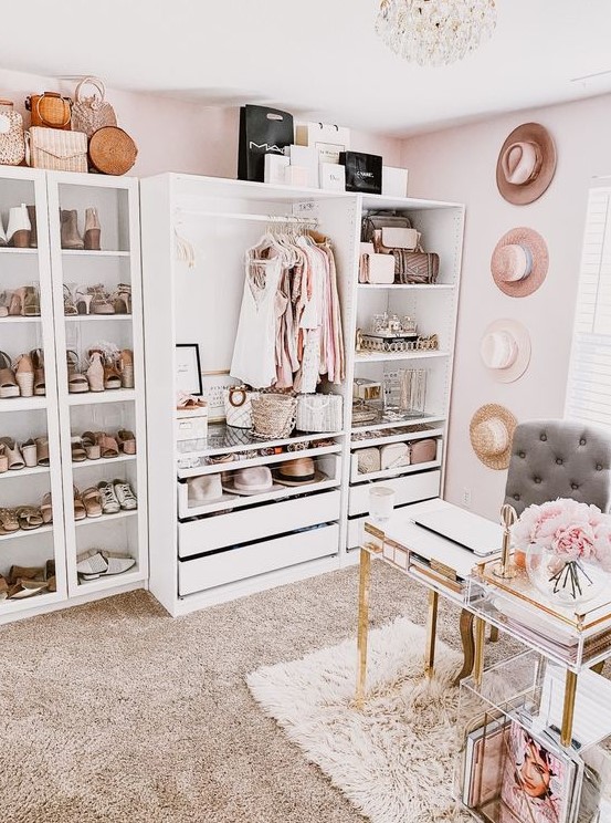 a girlish cloffice with a white makeshift closet, hats on the wall, a crystal chandelier, a catchy acrylic desk and a storage unit