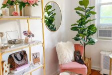 a glam and feminine cloffice with a large gold shelving unit, a glass desk, a pink chair, a beaded chandelier and potted plants