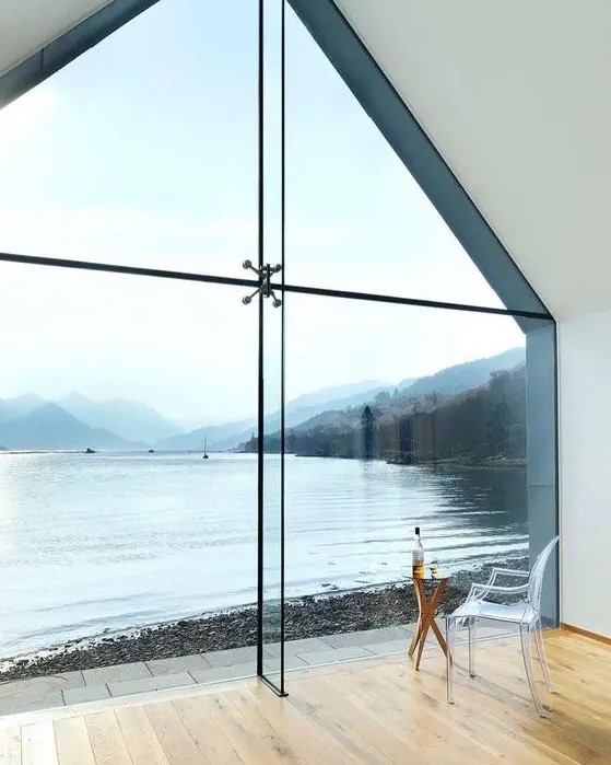 a gorgeous floor to ceiling window that repeats the shape of the house with its sloped roof and gives a beautiful view of the lake