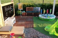 a gorgeous outdoor kids’ play space with a chalkboard, a pallet sofa with pillows, a pool with balls, colorful toys and a sandbox