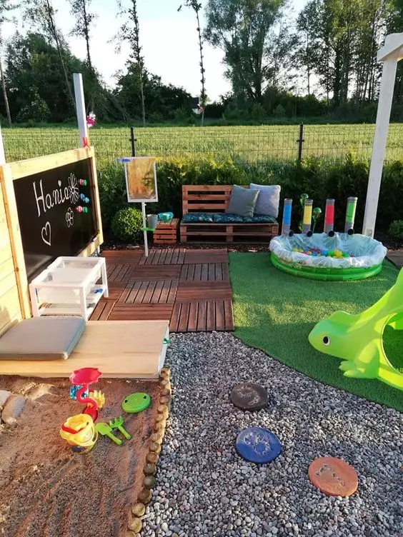 a gorgeous outdoor kids' play space with a chalkboard, a pallet sofa with pillows, a pool with balls, colorful toys and a sandbox