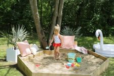 a hexagon sandbox with pink and white pillows, potted plants and even a dove float is a cool nook for playing