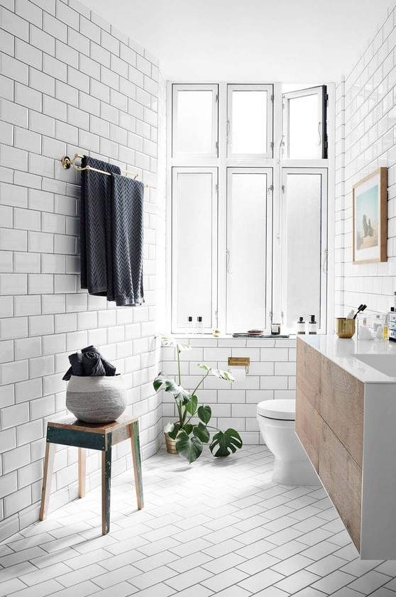 a light-filled Scandinavian bathroom clad with white subway tiles, a wooden floating vanity, wooden furniture and potted plants