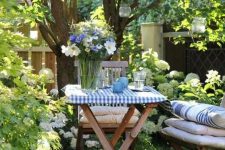 a little garden dining space on a green lawn, under the trees, with hanging candleholders and gold wooden chair plus cool textiles
