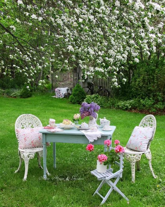 a little vintage tea space under the trees, with a blue table and vintage chairs plus floral porcelain