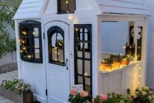 a lovely black and white kids’ playhouse with lights, potted plants and blooms, a black rug is a magical space to be