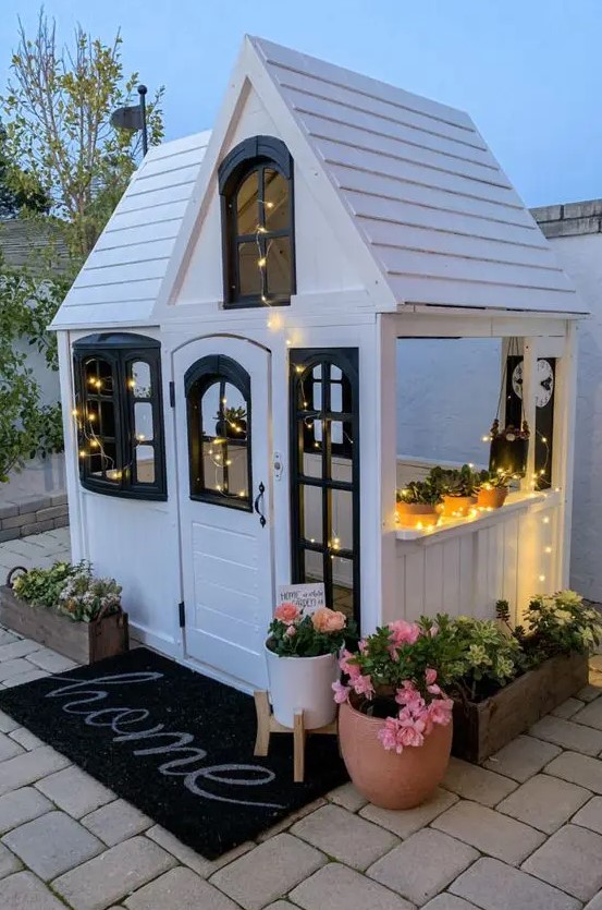 a lovely black and white kids' playhouse with lights, potted plants and blooms, a black rug is a magical space to be