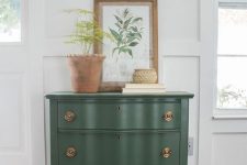 a lovely green vintage dresser with copper knobs, with a potted plant and a botanical poster will be a nice piece for a mid-century modern or rustic space