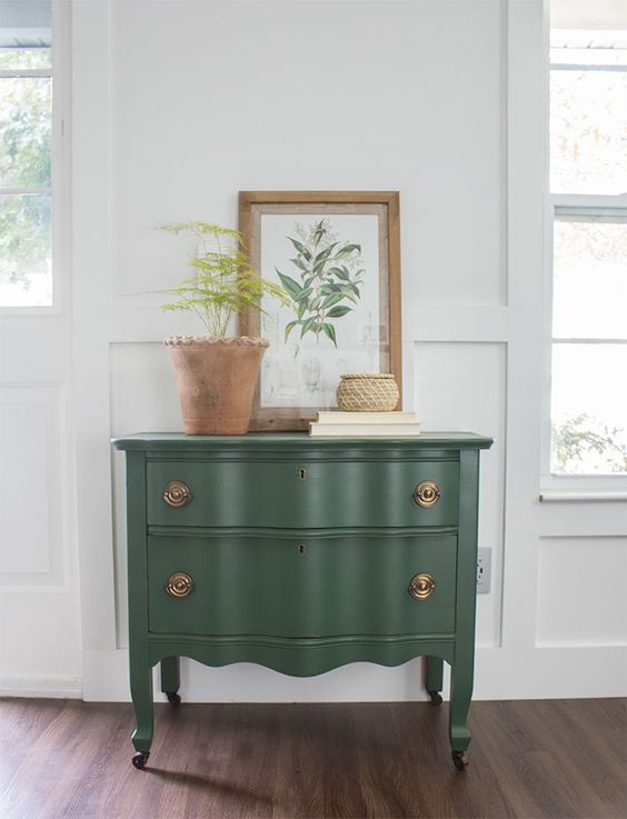 a lovely green vintage dresser with copper knobs, with a potted plant and a botanical poster will be a nice piece for a mid-century modern or rustic space